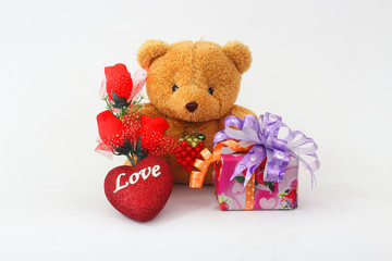 Brown teddy bear with a red rose and a gift box on a white background.