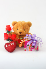 Brown teddy bear with a red rose and a gift box on a white background.
