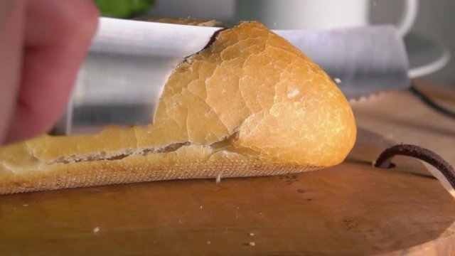 Slow motion of crumbs flying from the knife cutting freshly baked baguette