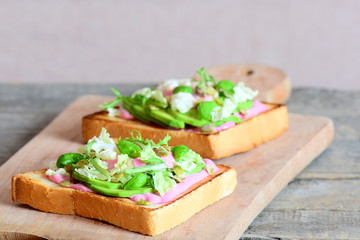Avocado sandwiches on wooden background. Toasted sandwiches made with sliced avocado, lettuce, basil and pumpkin seeds. Delicious healthy breakfast idea