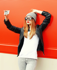 Fashion girl taking self-portrait on smartphone in city over red