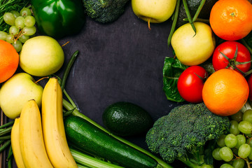 Food background of fresh fruit and vegetables bananas oranges apples grapes broccoli zucchini tomatoes on table Healthy lifestyle Top view Copy space in the middle