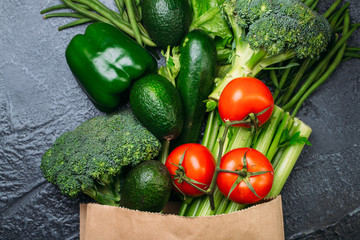 Food background of green vegetables broccoli romaine lettuce celery pepper zucchini tomatoes in shopping bag on black table Healthy lifestyle Top view Copy space