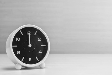 Closeup alarm clock for decorate in 12 o'clock on wood desk and wall textured background in black and white tone with copy space