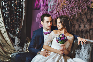 Wedding day. The bride and groom in a luxurious interior in lavender color. Wedding emotions. Beautiful bride and elegant groom at the ceremony.