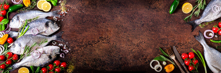Fresh uncooked fish, dorado, sea bream with lemon, herbs, vegetables and spices on rustic background. Top view. Banner