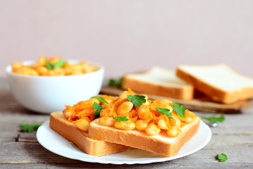 Homemade open sandwiches with baked white beans. Beans baked with carrots, garlic and tomato sauce in a bowl, bread slices, fresh parsley on a rustic wooden table. Vegetarian or vegan sandwiches