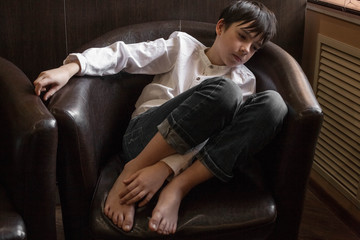 Boy in white shirt sitting in a chair. young boy imposingly placed in a leather couch. boy in shirt and jeans. Teenager relaxing in a cafe   © vetaka