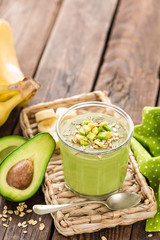 Avocado and banana smoothie with oats with ingredients in glass jar on wooden background, healthy eating