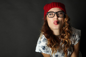 Funny girl shows tongue in a red cap on a black background.