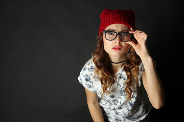 Funny girl posing in glasses and red hat on a black background.