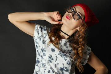 Funny girl posing in glasses and red hat on a black background.