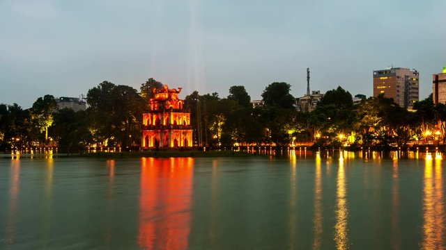 Hanoi, Vietnam time-lapse at sunset. Illuminated Turtle Tower at Hoan Kiem Lake in Hanoi, Vietnam. Tree at the background at night