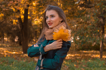 young girl with leaves in hand worth in autumn Park and looks away