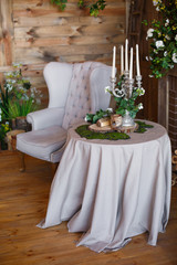 spring arbor, overgrown with greenery. A cozy corner with a soft arm-chair, a table, candles. Rustic style. Wooden interior with greenery