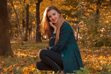 beautiful young girl in a black cloak sits on  lawn in autumn Park