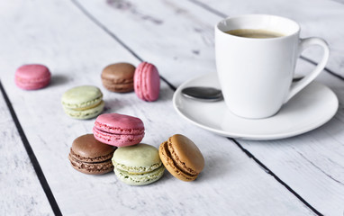 Delicious colorful macaroons with cream and coffee cup. Coffee break scene with macaroon candy and selective focus.