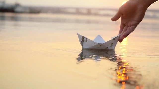 Man's hand launches paper boat on the water and pushing it away during beautiful sunset with reflection sun in the sea in slowmotion. 1920x1080
