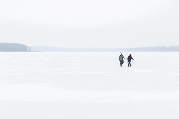 Fototapeta na wymiar Two anglers going to fishing on the lake ice in winter day. Fisherman.