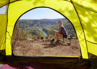 Young blonde woman tourists in camp on cliff over river and fore