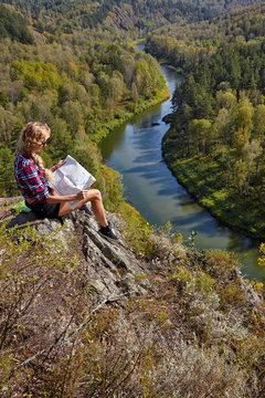 Young blonde woman tourist  sitting on a cliff with map in hands