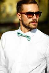 Handsome hipster model man in stylish summer clothes posing on street background in sunglasses