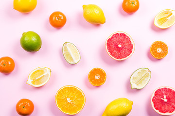 Several kinds of whole and cut citrus on a pink background