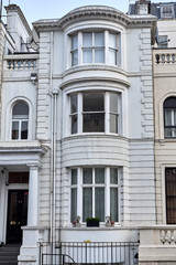 Fototapeta na wymiar Narrow building with bay windows in an ornamented facade with ashlar walling, pillars and decorated parapets, in London city