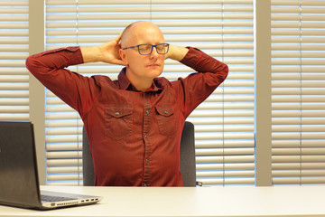 middle age balding man relaxing neck - stretching arms - short break for exercise on chair in office