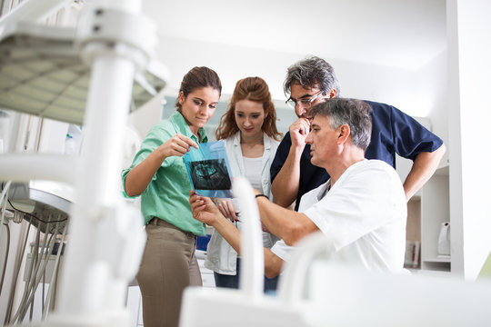 A group of dentists attentively examines X-ray images of a patient's teeth, ensuring precise diagnoses and comprehensive dental care.