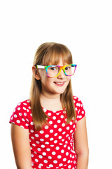 Studio portrait of adorable little 9-10 year old girl, wearing rainbow eyeglasses and red polka dot dress, standing against white background