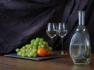 Bottle of white wine in a fancy bottle, two glasses of wine and fruits.
