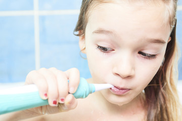 Close up of cute little girl in a bath and cleaning her teeth with electrical toothbrush against...