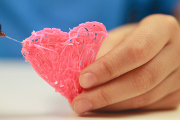 Kids hand hold heart which is made with 3D pen. Top view. Copy space for text. Selective focus
