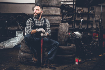 A man sits on an old tire in a garage.