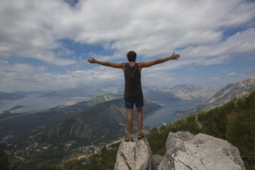 A young man sitaing over the sea at the rock and contemplating beautiful Kotor bay in Montenegro