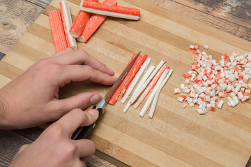 Hands cutting crab sticks on the wooden board in the kitchen. Healthy eating and lifestyle.