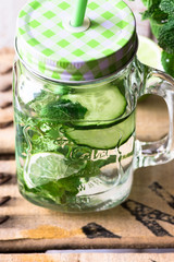 Jar mug with refreshing detox cucumber water with fresh mint and lime, wood background, outdoors, spring