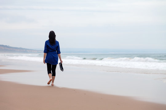Young woman walking away alone in a deserted beach on an Autumn day.