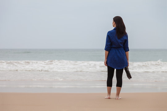 Lonely and depressed woman standing in front of the sea in a deserted beach on an Autumn day.