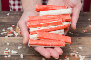 Hands holding crab sticks on the wooden table in the kitchen. Healthy eating and lifestyle.