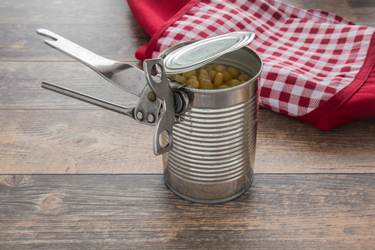 Old opener open to metallic can on the table in the kitchen. Canned corn in the can. Healthy eating and lifestyle.