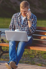 Obraz premium A young male businessman with a laptop and telephone. Remote work outdoors