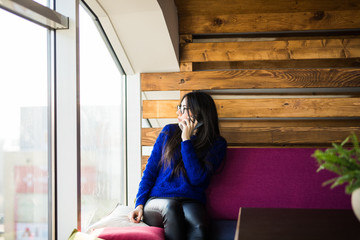 Young lady text sms in phone near window on sofa.