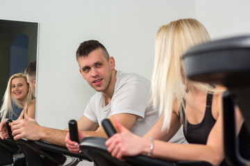 Obraz premium Young man and woman biking in the gym, exercising legs doing cardio workout cycling bikes