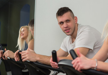 Fototapeta na wymiar Young man and woman biking in the gym, exercising legs doing cardio workout cycling bikes