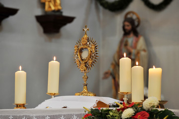 Monstrance and four white candles on the altar with Jesus' statue in the background.