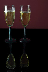 Two glasses of champagne on black table with reflection.