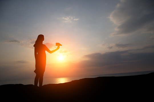 silhouette of a girl at sunset let a paper plane