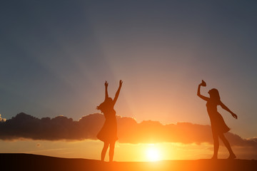 two girls dancing silhouette against the backdrop of a beautiful sunset and sea